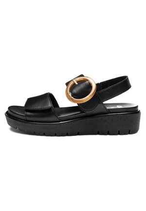 Black platform sandal with thick sole, adjustable strap with large round tan buckle, and open toe on white background.