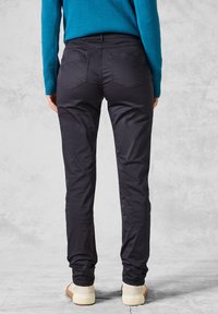 Un pantalon noir slim, avec une texture lisse et des poches standard, associé à un pull bleu et des chaussures de couleur claire.