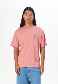 Blush pink cotton t-shirt with short sleeves, round neck, featuring a geometric design in blue and orange on the left chest area.