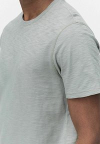 Ljusgrå t-shirt med kort ärm, tillverkad av strukturerad tyg med ett subtilt mönster, med rund halsringning och sydda detaljer på ärmarna.