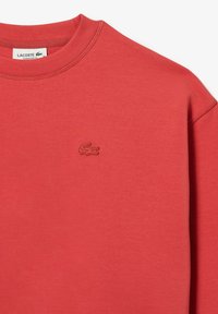 Röd sweatshirt i mjukt tyg med ribbad rund halsringning, med en broderad logotyp på vänster bröst. Oversized passform.