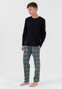 Czarny longsleeve połączony z zielonymi, czarno-białymi w kratkę spodniami do piżamy. Materiał wydaje się miękki, o luźnym kroju i bocznych kieszeniach.