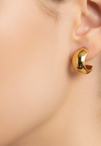 Orecchino a cerchio in oro con design aperto e curvo. Superficie liscia e riflettente. Aspetto leggero e forma moderna e minimalista.