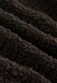 Tissu texturé marron foncé avec un motif ondulé tridimensionnel, présentant des fibres douces et bouclées qui créent de la profondeur et de l'intérêt visuel.