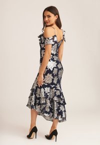 Navy blue dress with silver floral patterns, ruffled sleeves, and a tiered hemline. Worn with black high-heeled shoes.