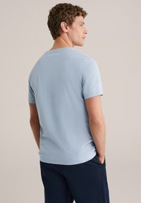 Világoskék rövid ujjú póló hátulnézetből, környakú és puha pamut anyagból készült. Sötétkék nadrággal viselve.