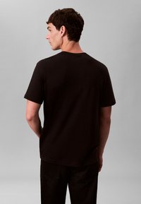 T-shirt en coton noir avec col rond et manches courtes, présentant une coupe décontractée et une texture lisse, vu de dos.