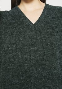 Mörkgrön stickad tröja med V-halsdesign, strukturerad tyg och ett mjukt, något ludet utseende.