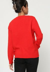 Pull rouge avec un col rond et des manches longues, fabriqué dans un tissu doux et texturé. Il présente un ourlet et des poignets côtelés.