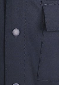 Navyblauwe jasstof met een gladde textuur, voorzien van een grote knop en een klein borstzakje met zichtbare stiksels.