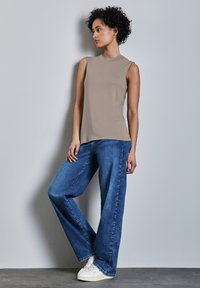 Top beige senza maniche, jeans in denim blu larghi e sneakers bianche. Tessuto morbido con scollatura rotonda e gambe dei pantaloni ampie.
