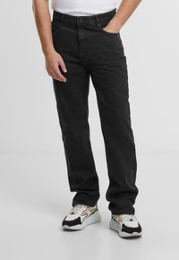 Jeans din denim negru cu o croială dreaptă, având cinci buzunare, închidere cu nasture și o suprafață texturată. Purtați cu pantofi sport multicolori.