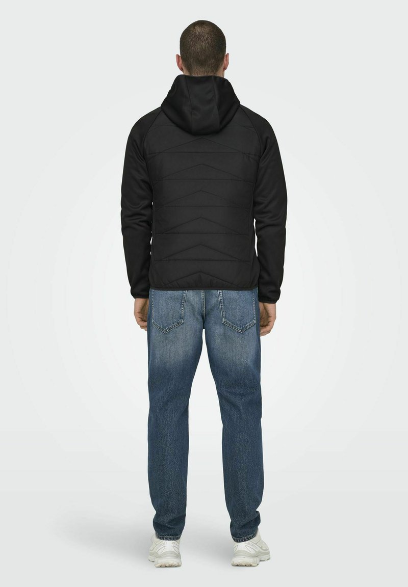 Veste à capuche noire avec un design matelassé, associée à un jean en denim bleu. Le tissu semble lisse, mettant en avant une esthétique moderne et minimaliste.