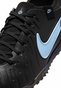 Pantofii sport negri au un upper din piele texturată, cu un swoosh de accent albastru și șireturi negre. Au o talpă din cauciuc cu tracțiune pronunțată.