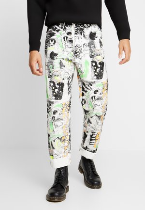 White pants with black, green, and orange graffiti-style skull and abstract art print, paired with rolled cuffs and black lace-up boots.