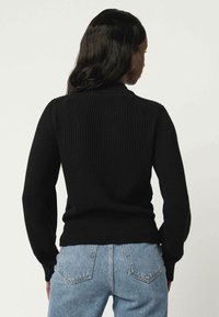 Schwarzer, gerippter Pullover mit langen Ärmeln und einem engen Halsausschnitt, kombiniert mit hellblauen High-Waist-Jeans. Strukturiertes Strickmaterial.