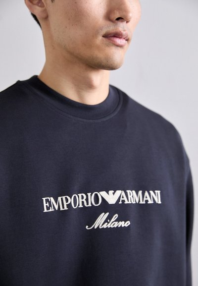 Sweatshirt bleu marine en mélange de coton avec un col rond. Doté d'un logo brodé blanc "EMPORIO ARMANI Milano" sur le devant.