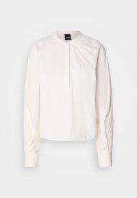 Blouse blanche à manches longues avec col mandarin et fermeture par un seul bouton à l'avant, présentée sur un fond clair uni.