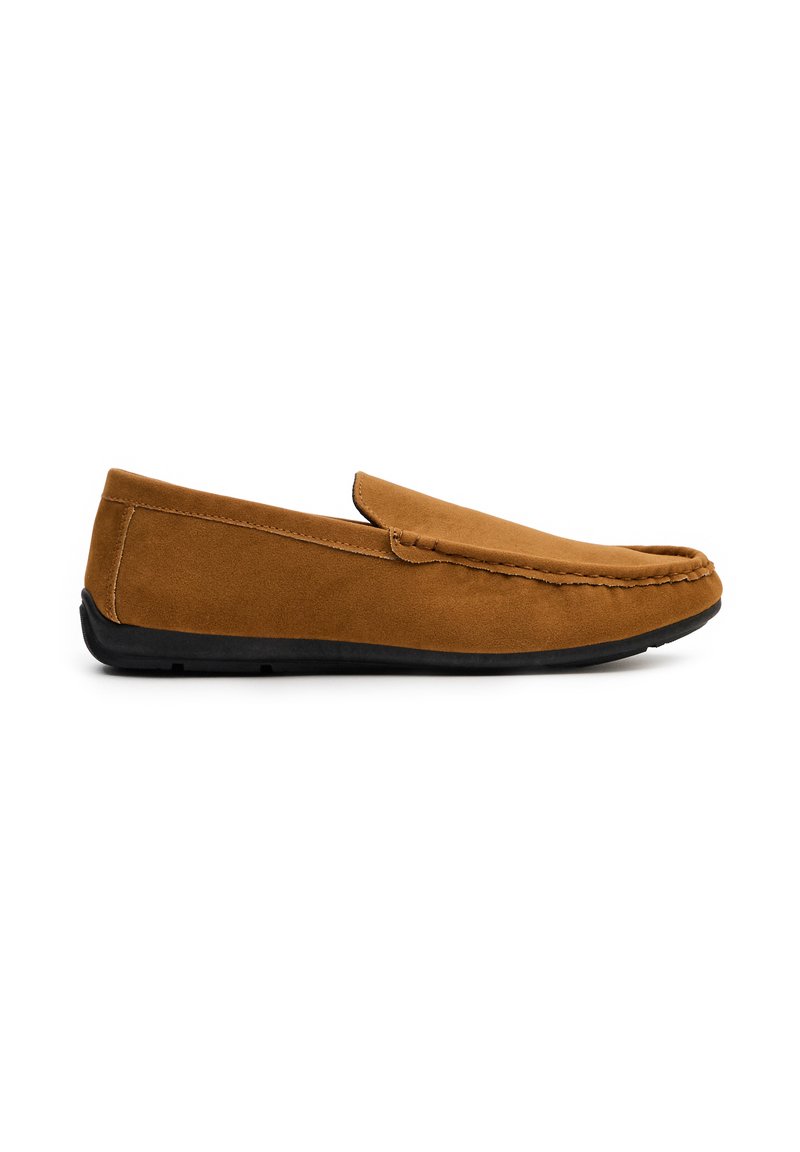 Mocasines de ante marrón sin cordones con una suela de goma negra plana. Textura suave, punta redondeada y costuras visibles a lo largo del borde superior.