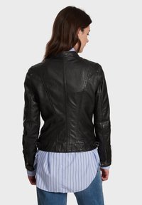 Crna kožna jakna s prilagođenim dizajnom, teksturiranom završnom obradom i ukrasnim kopčama u struku. Ima strukturirane šavove i duge rukave.