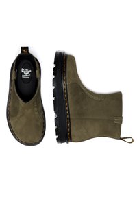 Botines de cuero verde oliva con un acabado texturizado, suela de goma negra y costuras amarillas contrastantes. Incluyen una lengüeta para facilitar su colocación.