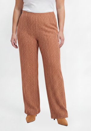 Bruine wijde broek met visgraatmotief, gedragen met tan puntige hakken en een wit mouwloos topje tegen een effen achtergrond.
