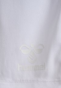 Vit tyg med en slät textur och en reflekterande logotyp av en stiliserad vingad figur med ordet "hummel" nedanför.