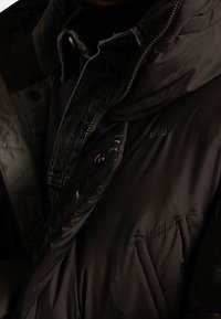 Kurtka puchowa z ciemnobrązowego nylonu o pikowanej strukturze, z wysokim kołnierzem, zamkami błyskawicznymi i warstwowym designem z denimu pod spodem.