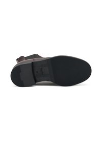 Suela de zapato de goma negra con superficie texturizada, presenta un leve tacón elevado, logo en relieve y parte superior de piel lisa en burdeos.