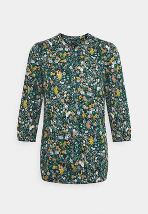 Blouse verte à manches longues avec un imprimé floral dense en jaune, blanc et orange, avec un col rond et des boutons à l'avant.