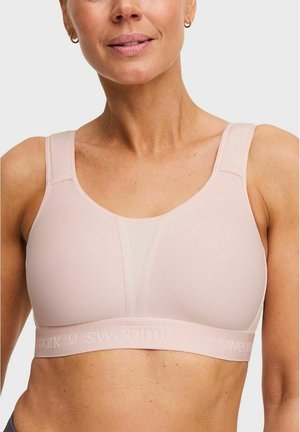 Vrouw draagt een lichtroze sportbeha met brede bandjes en mesh-detail in het midden, waarbij het bovenlichaam en de nek zichtbaar zijn.