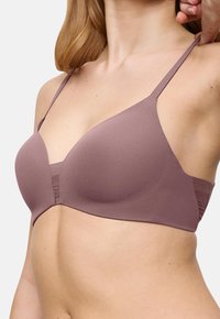 Γυναίκα ρυθμίζει τη λουρίδα ενός λείο, μωβ, χωρίς σύρμα σουτιέν με λεπτές ρυθμιζόμενες λουρίδες και αδιάκοπη σχεδίαση.