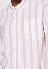 Button-up shirt with pink and white vertical stripes, made of cotton, featuring a single chest pocket and a classic collar style.