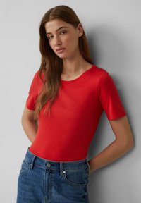 Rode t-shirt met korte mouwen en een ronde halslijn, gemaakt van een gladde stof, gecombineerd met hooggegarende blauwe denim jeans.