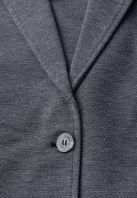 Blazer gris texturé à l'avant avec des revers et un seul bouton gris fermé près du centre.