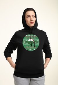 Sudadera negra con capucha que presenta un gráfico circular verde con el texto "Silent Night Jedi Knight" y patrones festivos, hecha de tela suave y con un corte relajado.