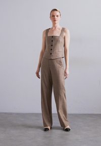 Καφέ γωνιακό γιλέκο από λινό μίγμα και κοστούμι με φαρδιές παντελόνες. Το γιλέκο διαθέτει τετράγωνη λαιμόκοψη, τέσσερα μεγάλα κουμπιά και κομψή σιλουέτα.