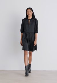 Rochie scurtă neagră cu mâneci puff și decolteu în formă de cheie, având o croială lejeră și o textură moale, asortată cu cizme până la gleznă.
