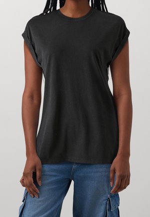 Personne portant un t-shirt noir à manches courtes à revers et un pantalon cargo en denim bleu, se tenant avec les bras détendus sur les côtés.