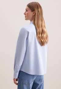 Camicia a righe blu chiaro con maniche lunghe, dotata di polsini con bottone e una vestibilità comoda. Dettaglio posteriore mostra un design a yoke.