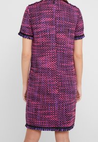 Šaty s krátkým rukávem vyrobené z tkané látky se vzorem v odstínech růžové, fialové a černé, s třásněmi na lemu a strukturovaným střihem.