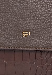 Brązowy portfel ze skóry o fakturze, z gładkim wykończeniem, ozdobiony złotym logo i akcentem z wzorem krokodyla na dolnej krawędzi.