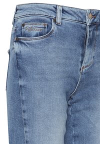 Jeans de denim azul claro con un pequeño bolsillo frontal que presenta "Petit Tours" bordado en hilo marrón.