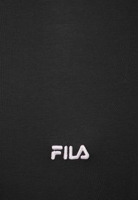 Camiseta de tela negra con textura suave, que presenta un logo bordado en blanco de "FILA" situado en la parte inferior derecha. Diseño simple, sin patrones adicionales.