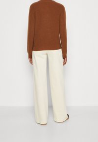 Suéter marrón de punto con textura acanalada, combinado con pantalones de pierna ancha en color crema. El suéter tiene un escote redondo y mangas largas.