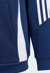 Marineblaue Sweatshirt mit weißen Seiteneinsätzen, ausgestattet mit einer Fronttasche und gerippten Bündchen. Weiche Textur, sportliches Design.