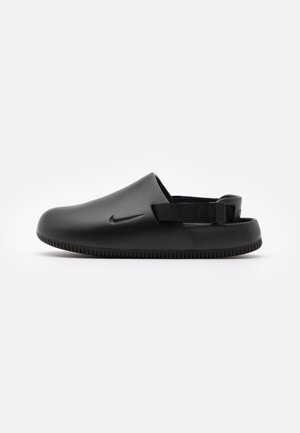 Sabot noir à enfiler avec semelle texturée, bride arrière réglable et logo Nike sur le côté, sur un fond clair uni.