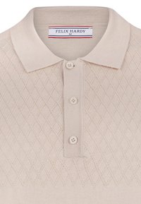 Beżowa dzianinowa koszulka polo z wzorem w romby, miękkim kołnierzykiem i trzema kremowymi guzikami. Metka z napisem "FELIX HARDY" w czerwonych i niebieskich akcentach.