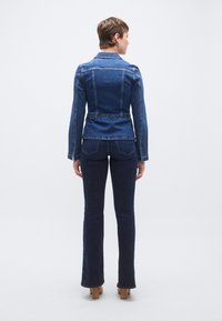 Τζιν μπουφάν με εφαρμοστό σχέδιο, σκούρο μπλε χρώμα, κλασικό γιακά και τονισμένες ραφές, σε συνδυασμό με σκούρα τζιν με φουσκωτά μπατζάκια κα ι ψηλοτάκουνα παπούτσια.