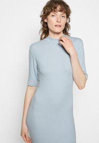 Vestido azul claro canelado com gola alta e mangas curtas, silhueta ajustada, textura suave e detalhes mínimos.